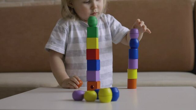 Little girl playing wooden geometrical figures on the table. Sorting rainbow cubes. Hand held Close Up Shot.