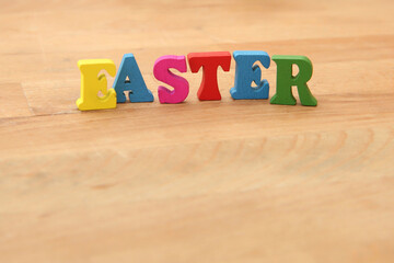 Easter spelt in colourful wooden letters against a natural wooden beige background.