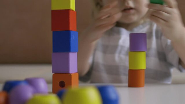 Little girl playing wooden geometrical figures on the table. Sorting rainbow cubes. Hand held Close Up Shot.