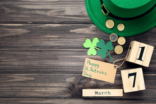 Paper clover leafs, coins, hat with calendar and text Happy St.Patrick's Day on wooden table