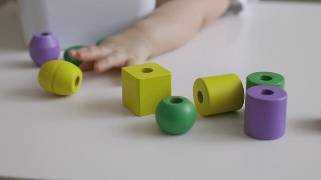 Little girl playing wooden geometrical figures on the table. Sorting rainbow cubes. Hand held Close Up Shot.