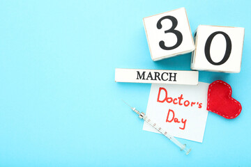 Text Doctor's Day with cube calendar, red heart and syringe on blue background