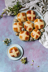 Homemade Easter traditional hot cross buns on ceramic plate with blossom cherry branches, quail eggs, textile over blue texture background. Flat lay, space