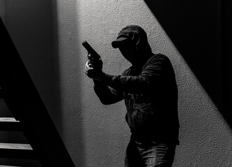 Armed criminal wearing hoodie and cap holds a gun