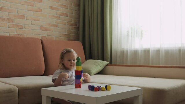 Little girl playing wooden geometrical figures on the table. Sorting rainbow cubes. Medium shot.