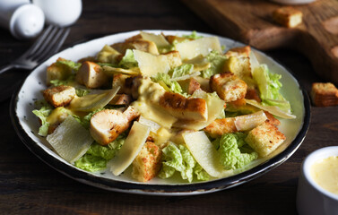 Caesar salad with lettuce, chicken and sauce on a wooden background.