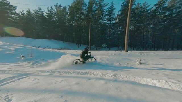 Cyclist in Black Clothes, Helmet and Snow Glasses Riding on Electric Bike in the Snow in Winter Forest. E-Bike Riding and Drifting at Cold Sunny Day - Super Slow Motion