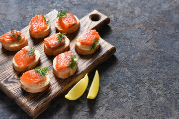 Toast from bread with butter and salmon on a wooden board on a concrete background. Breakfast. Fish canapes on the table.