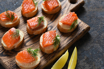 Toast from bread with butter and salmon on a wooden board on a concrete background. Breakfast. Fish canapes on the table.