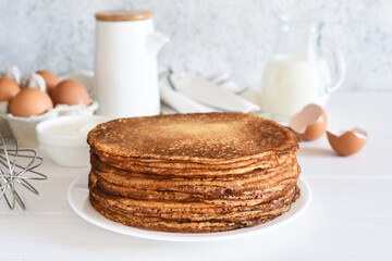 A stack of pancakes and sour cream whisk, eggs and milk on a light background.
