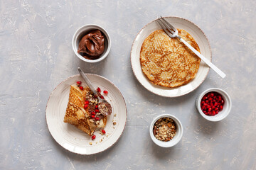 Thin pancakes on plate with pomegranate, chocolate and walnuts on light background. Top view, close-up