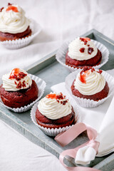 Homemade Red velvet cupcakes with whipped cream on wooden tray, white napkin with ribbon on white linen table cloth.