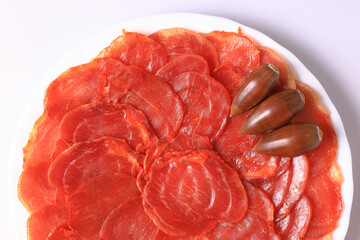 Portion of acorn-fed Iberian loin decorated with acorns on a white plate and with a white background