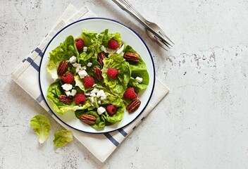 Fresh green salad with raspberry, goat cheese and caramelized pecans on rustic wooden table. Flat layot,copy space
