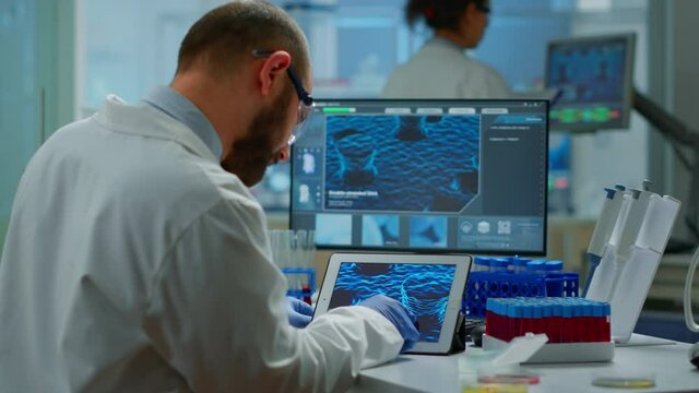 Biochemist checking manifestations of virus looking in tablet with special software in chemistry laboratory. Group of doctors examining vaccine evolution using high tech researching diagnosis