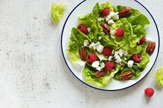 Fresh green salad with raspberry, goat cheese and caramelized pecans on rustic wooden table. Flat layot,copy space