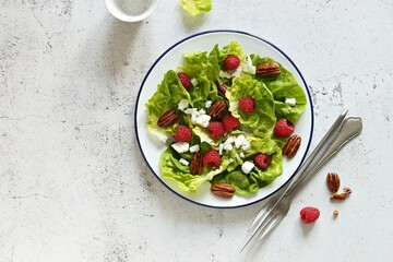 Fresh green salad with raspberry, goat cheese and caramelized pecans on rustic wooden table. Flat layot,copy space