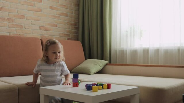 Little girl playing wooden geometrical figures on the table. Sorting rainbow cubes. Medium shot.