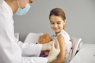Happy little girl getting a shot at doctor's office. Male nurse giving vaccine injection to smiling...