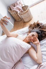 Obraz na płótnie Canvas Sleepy woman taking selfie on smartphone on blurred foreground on bed