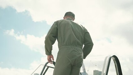 pilot in a green military suit climbs the wing of his single-engine propeller plane into the cockpit to take off - Powered by Adobe