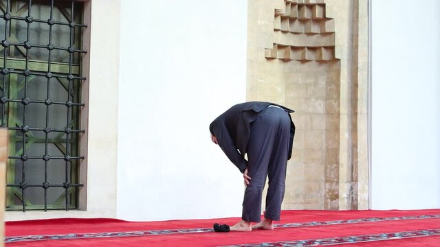 An old man praying a daily prayer on a porch of a mosque.