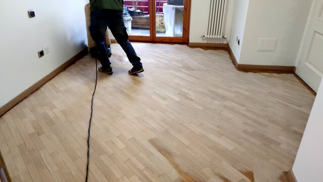 pad sander sanding hardwood floor in empty room. Man working to sand an old wooden floor to original raw wood.