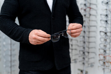 Showcase with spectacles in modern optics store on the background. Man`s hands with glasses. Closeup.