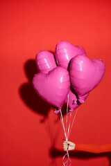 A female hand holds an inflatable purple heart-shaped balloons. Picture taken in the studio on a red background.