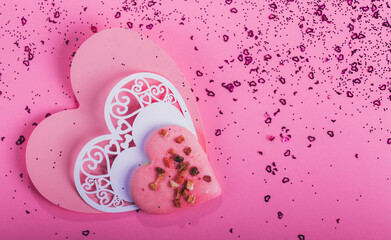 Heart shape cookie and paper hearts shaped cards on pink background