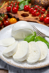 Cheese collection, eating. of white soft Italian cheese mozzarella, served with red cherry tomatoes, fresh basil leaves