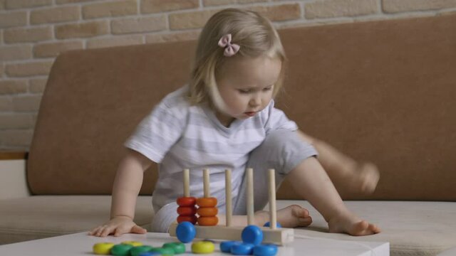 Little girl playing wooden education games on the table. Sorting rainbow wheels. Handheld Close Up Shot.
