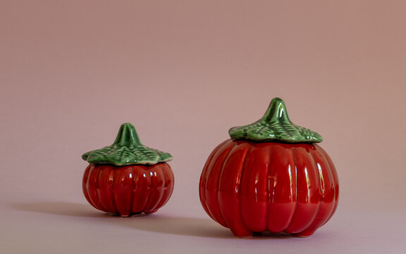Two pumpkins of different sizes in red color and green cap on a pink background. Utensil can be used to store rice, beans, flour, pasta, seasoning, food in general. Decoration accessory for kitchen.
