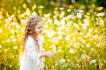 little beautiful girl playing on the lawn in summer with soap bubbles