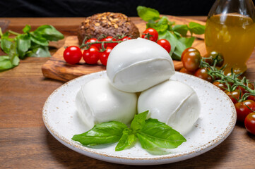 Cheese collection, white balls of soft Italian cheese mozzarella, served with red cherry tomatoes, fresh basil leaves