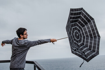 Young man with an umbrella turned around by the wind - obrazy, fototapety, plakaty