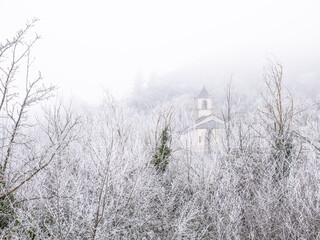 Church with slate roofs inside a frozen forest surrounded by fog
