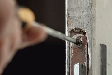 Screwdriver in male hands for repair old lock in wooden door