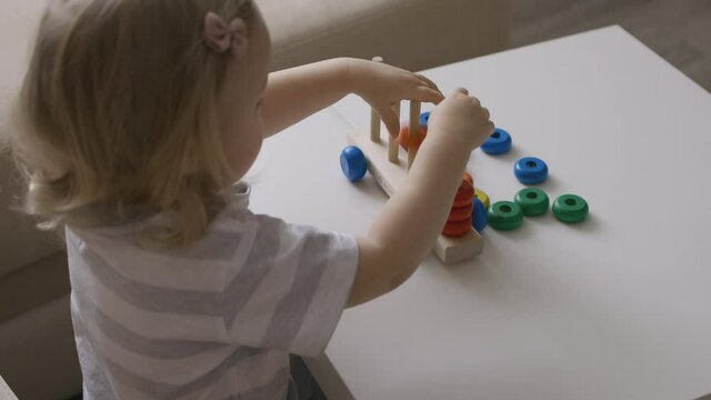 Little girl playing wooden education games on the table. Sorting rainbow wheels. Handheld Close Up Shot.
