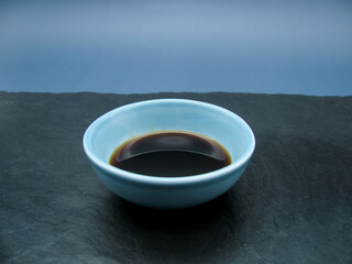 Fresh brown soy sauce in a blue bowl on a stone board and on a blue background.