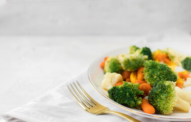 Mixed vegetables on a plate and a golden fork on light background. Free space