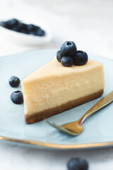slice of new york cheesecake with fresh blueberries on blue luxury plate and a golden fork on light background