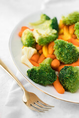 Mixed vegetables on a plate and a golden fork on light background