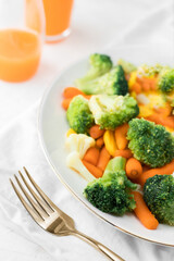 Mixed broccoli, cauliflower, carrot on a plate and a golden fork on light background