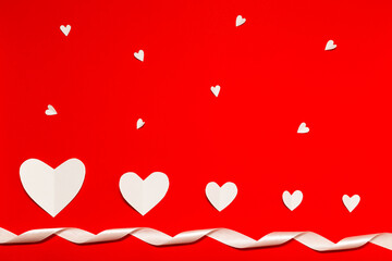 Obraz na płótnie Canvas White paper hearts with white color ribbon over the red background in flat lay style. Valentine's Day composition. Holiday concept.