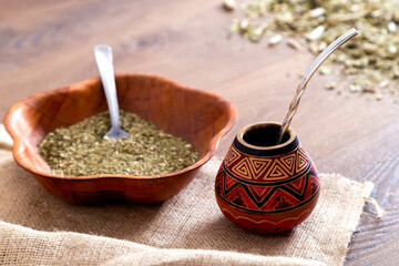 Traditional mate made of calabash over a wooden table with yerba mate scattered over it.