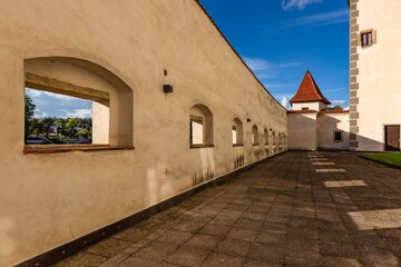 Jindrichuv Hradec, Czech Republic - September 26 2019: View of the surrounding wall with windows and little tower belonging to the castle. Tile paving on the ground. Sunny autumn day with blue sky.
