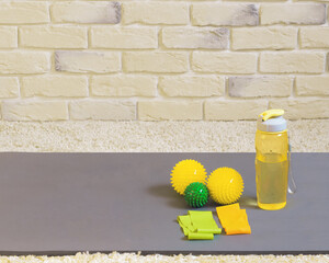 Fitness equipment on a yoga mat on a brick wall background. A sports bottle of water, training resistance rubber bands and massage balls. Copy space. Home fitness concept.