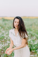 Naklejka na ściany i meble Portrait of a brunette girl with chamomile flowers. Freedom from pollen allergies and blooms. Enjoy the freedom of breath and the scent of flowers.