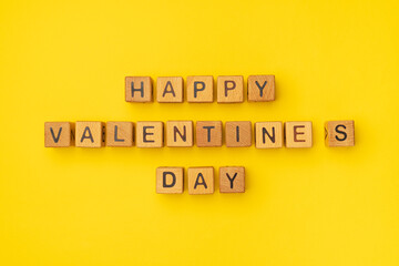 Wooden cubes with the phrase Happy Valentine's Day on an empty colorful yellow background. Words of...